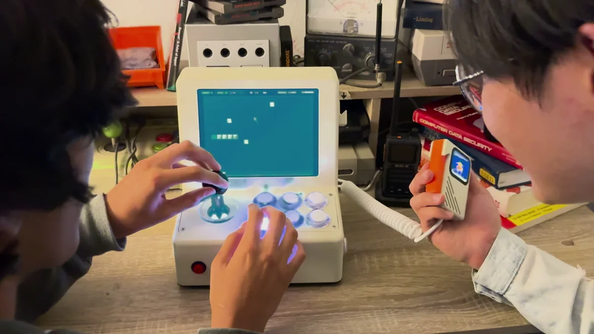 Two people playing VibeConsole together, using the arcade controls and handheld microphone.